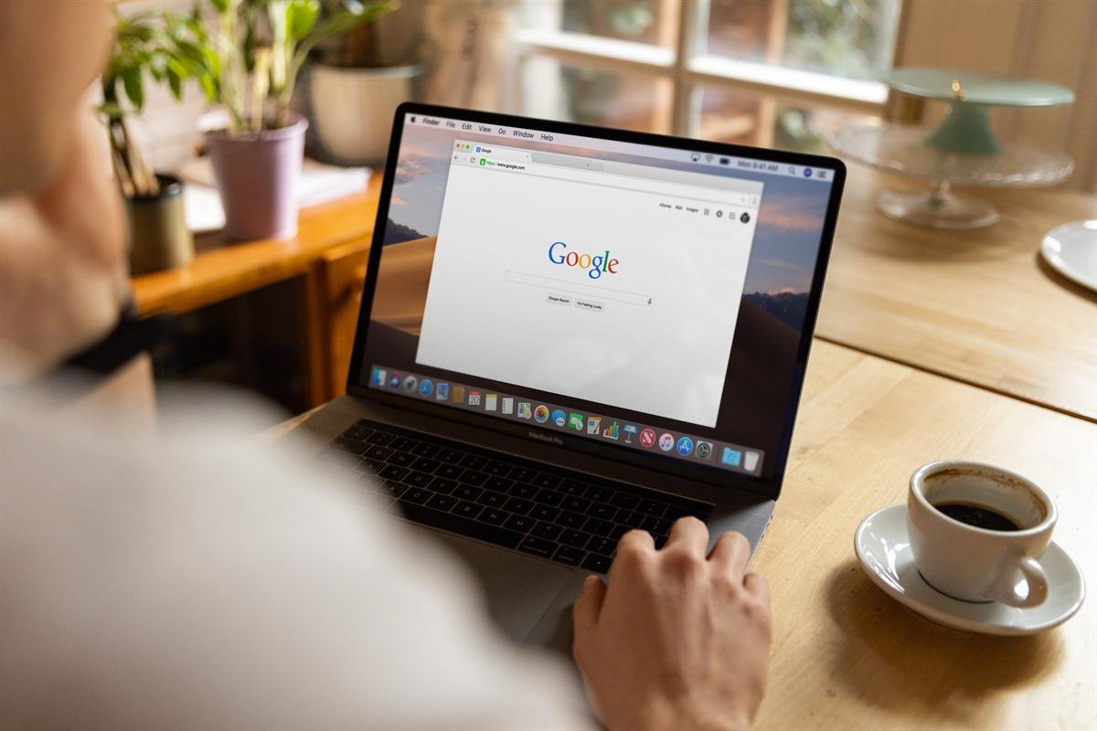 Person browsing Google on a laptop at a wooden table with coffee