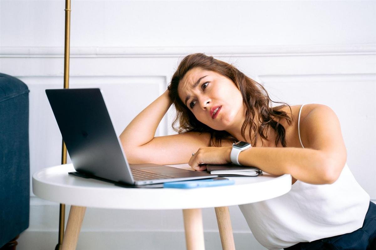 Frustrated person resting a hand on their head while looking at a laptop