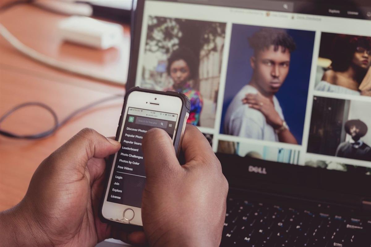 Hands holding a smartphone in front of a laptop, searching the web