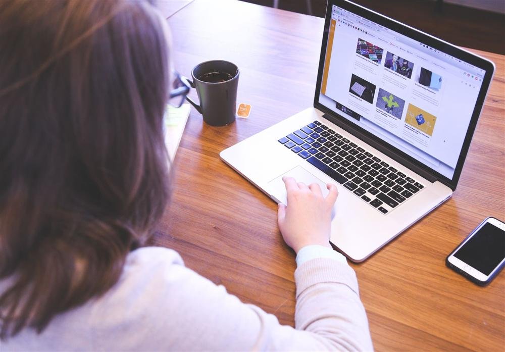 Person browsing a website on a laptop at a wooden desk with a smartphone nearby