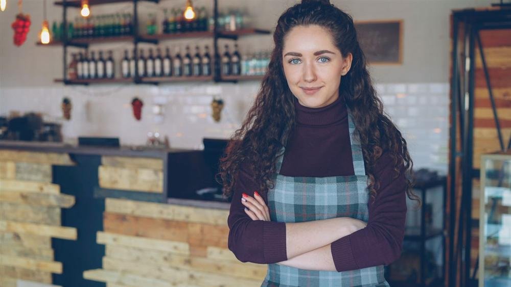 Café owner standing with arms crossed inside a cozy coffee shop