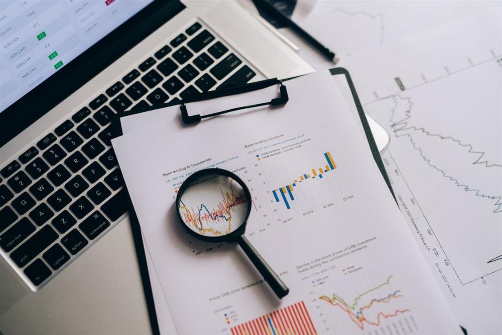 Overhead view of printed charts, a laptop and a magnifying glass on a desk