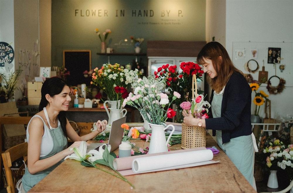 Two florists in aprons working with flowers and a laptop in a small shop